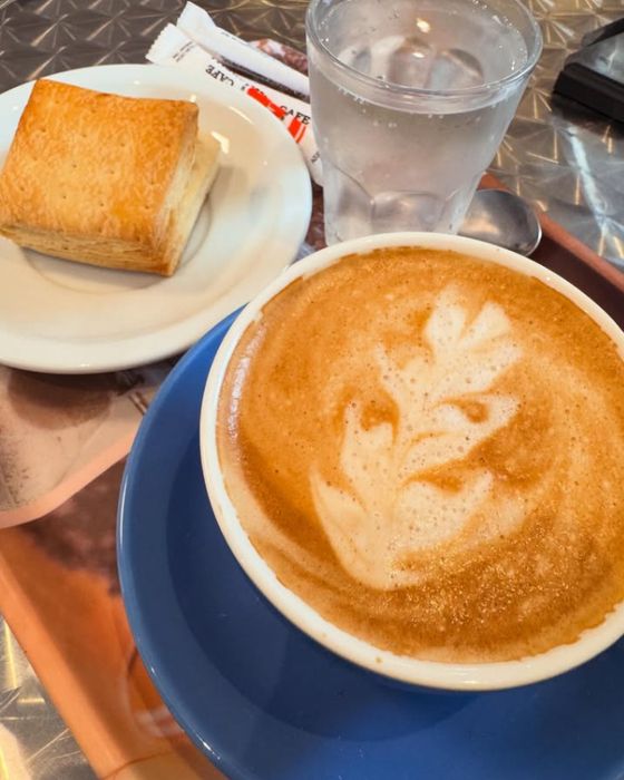 Café con latte art, vaso de agua y bocadito de hojaldre en la mesa