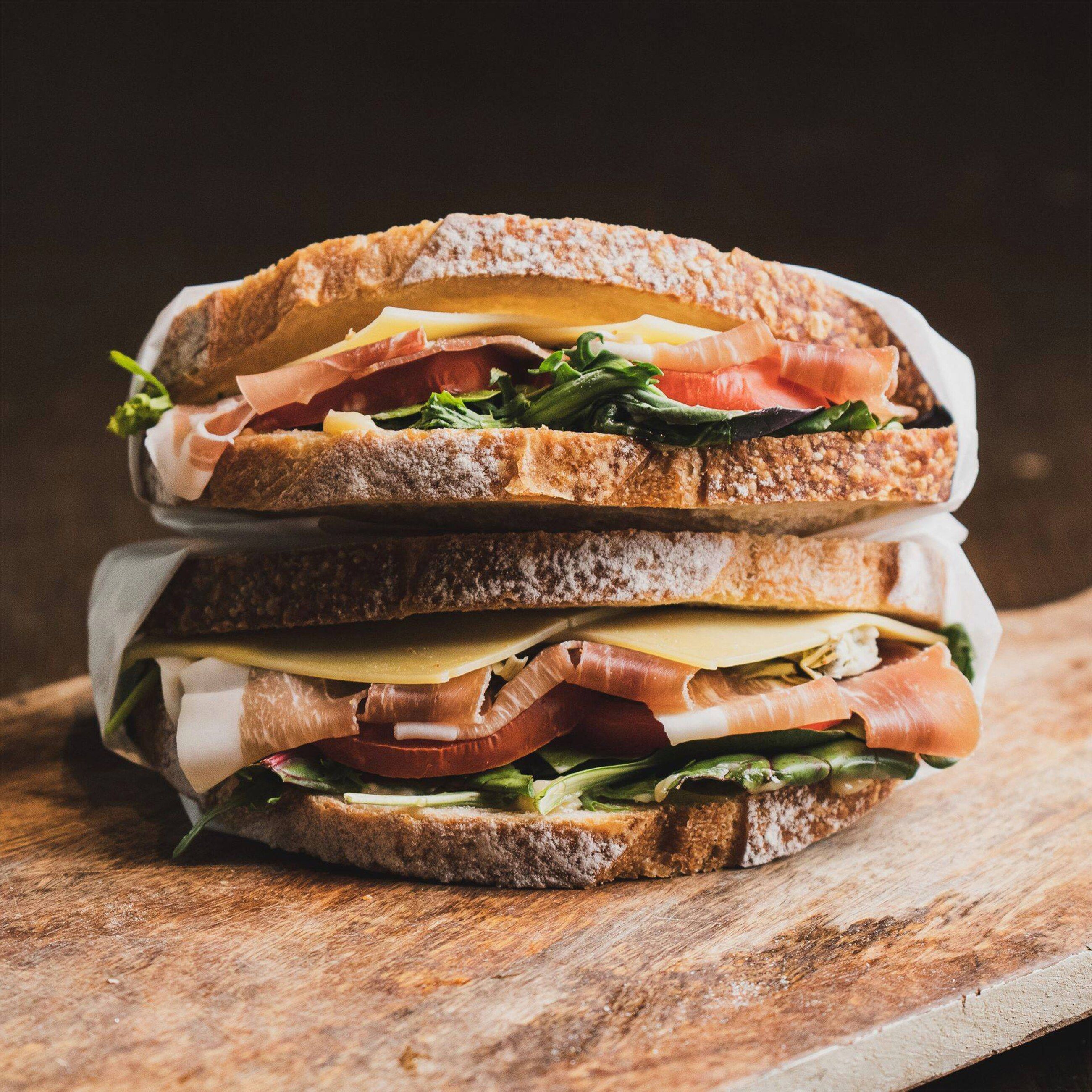 Sándwich de varias capas sobre una tabla de madera oscura, con luz cálida