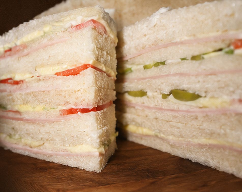 Corte de un sándwich de miga triple capa de Estrella de Belén: tres pisos de jamón, queso y tomate sobre una tabla de madera